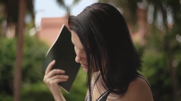 Close up of pretty brunette female standing outside and fanning with a notebook. Young brunette swea