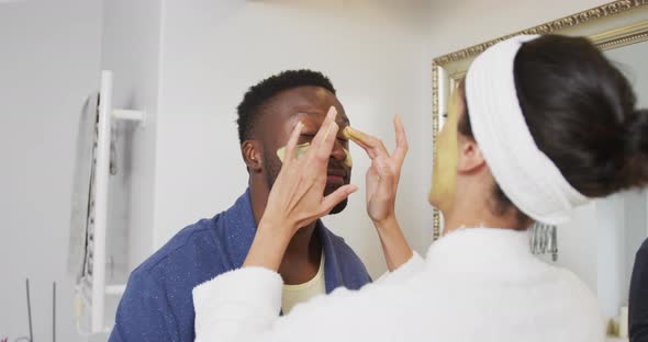 Happy diverse couple looking at each other and doing make up in bathroom