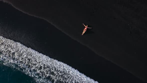 Top View of a Girl in a Red Swimsuit Lying on a Black Beach on the Surf Line. Coast of the Island of