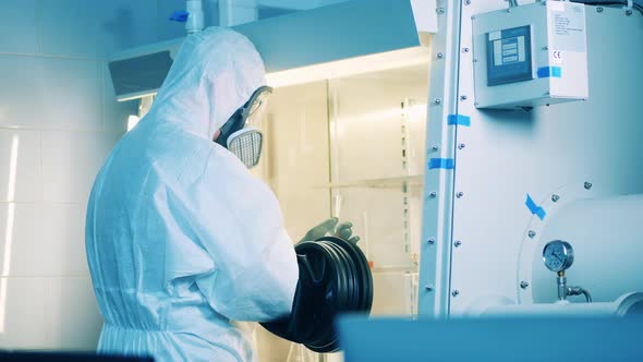 Lab Worker in a Hazmat Suit is Using a Vacuum Cabinet for Research