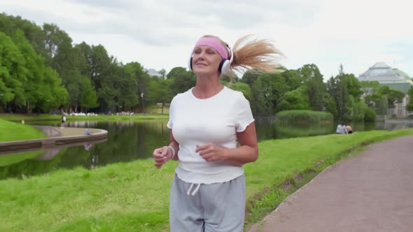 Smiling Middleaged Woman in Sportswear and Headphones Running in Park