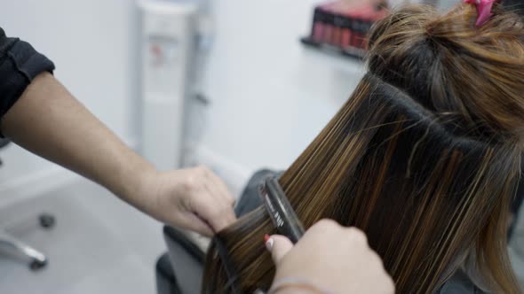 Close Up of Unrecognizable Hairdresser Using Hair Straightener on Client's Hair