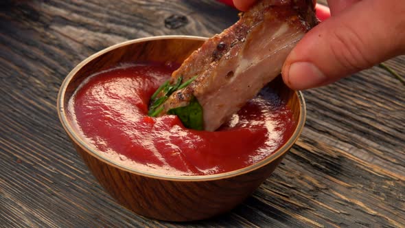 Closeup of the Juicy Grilled Ribs Dipped Into the Ketchup in a Small Bowl