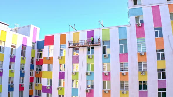 A Worker Paints A Building At A Height.