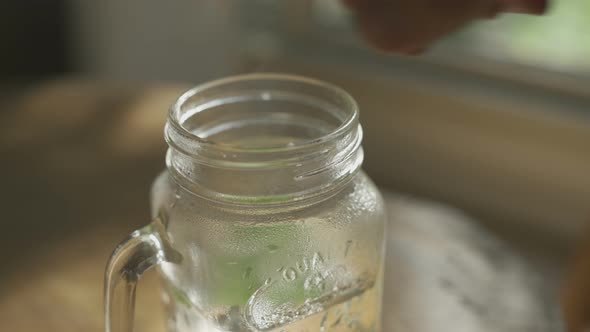 Adding mint and tea leaves into glass mug with boiling water