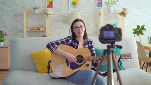 Young Woman Blogger Sitting on the Couch with a Guitar in His Hands in Front of the Camera