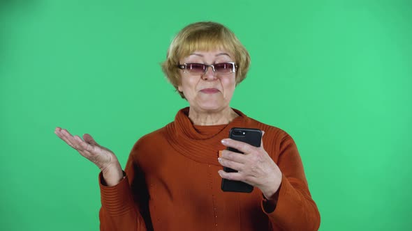 Portrait of Senior Woman Is Talking for Video Chat Using Mobile Phoneisolated Over Green Background.