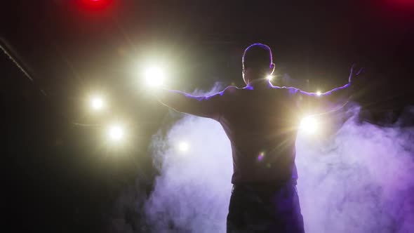 Showman Is Clapping Hands on Stage and Entertaining Audience in Spotlights, Back View.