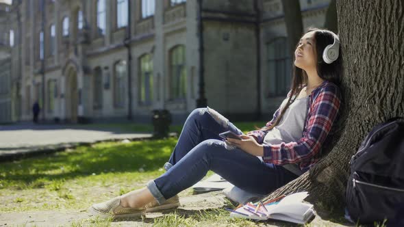 Female Student Sitting on Grass, Leaning Against Tree, Listening to Music, Relax