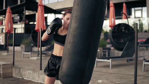 Attractive Athletic Female Boxer in Gloves Kicking a Punching Bag