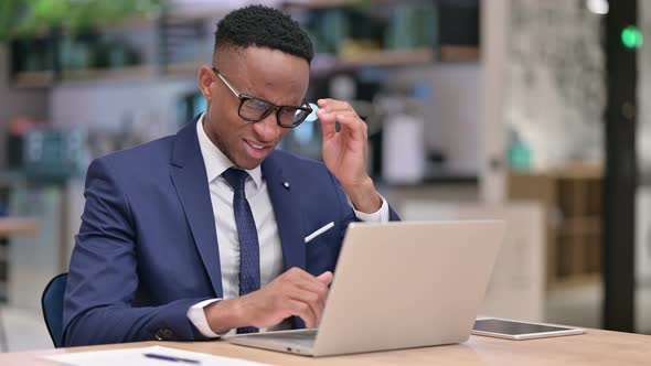 Stressed African Businessman with Laptop Having Headache in Office 