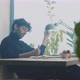 Young man sitting at table casually making notes while playing with plant - VideoHive Item for Sale