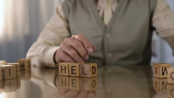 Senior Man Making Word Help of Wooden Cubes on Table, Parkinson Disease, Tremor