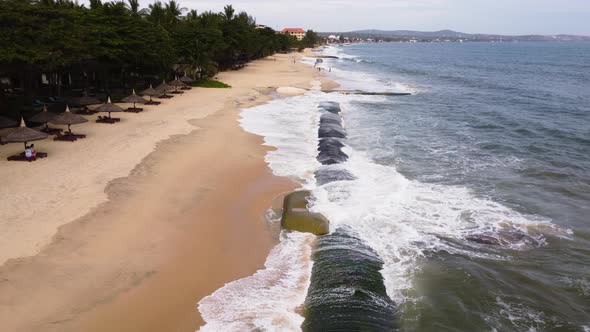 Man made geo tube protecting sandy beach from strong ocean waves, aerial fly over shot