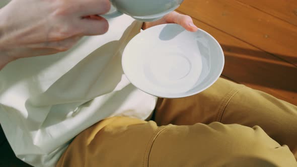 White cup of herbal tea with a saucer in female hands.