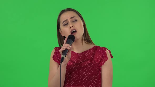 Portrait of Tender Girl in Red Dress Is Singing Into a Microphone and Moving To the Beat of Music