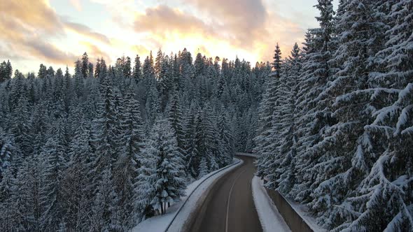 Aerial view of winter landscape with snow covered mountain hills and winding forest road in morning. alt