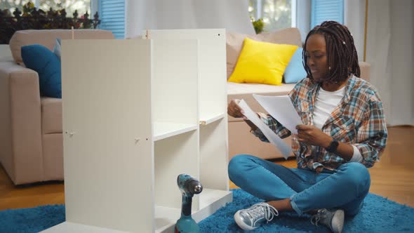 Young African Woman with Screwdriver and Instruction Assembling New Cupboard at Home