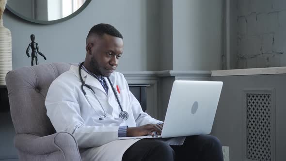 a Young AfricanAmerican Doctor is Working on a Laptop and Talking on the Phone