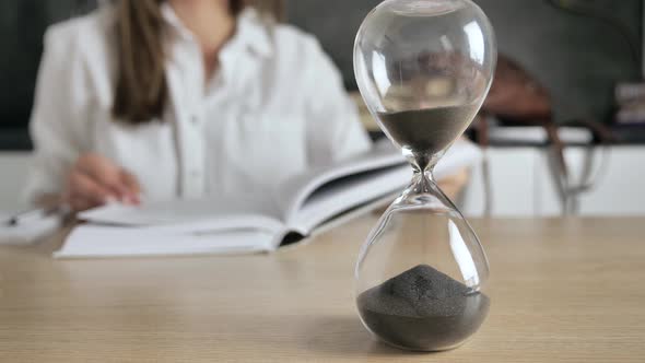 Hourglass Black Sand in a Transparent Flask is Poured Silhouette of a Girl Reading a Book Background