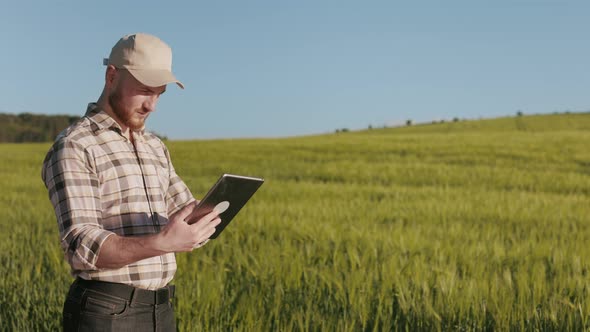 The Farmer is Standing Near the Field and Working with a Tablet