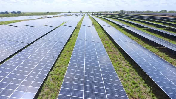 Solar panels lined up on photovoltaic farm, renewable energy; aerial push-in