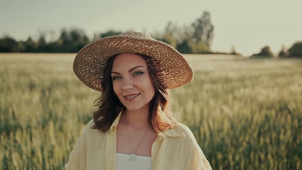 Portrait of Attractive Woman in Straw Hat in Fresh Green Wheat Field