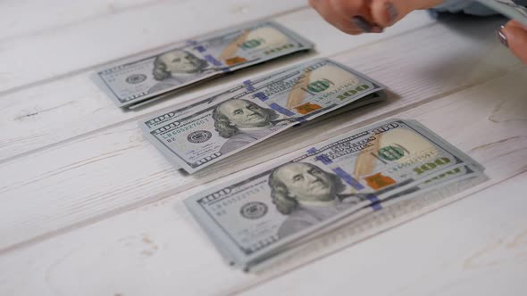 A Closeup of a Woman Counts Hundreddollar Bills on a Light Wooden Background