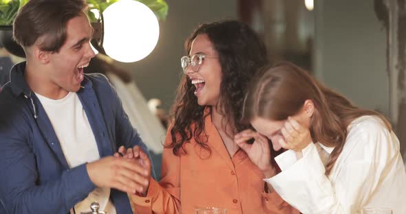 Close Up View of Young Woman in Glasses Joking and Hugging Her Friends in Modern Cafe. Multiethnic