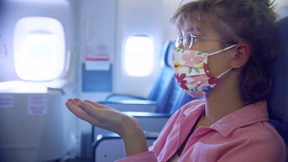 a Passenger on an Airplane in a Protective Mask is Applying an Antiseptic on Her Hands
