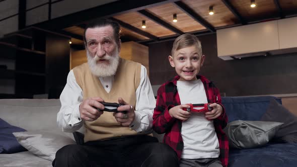 Bearded Man and His Teen Grandson which Having Fun Together at Playing Video Games 