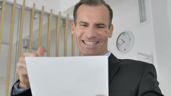 Middle Aged Businessman Celebrating Success While Reading Documents in Office