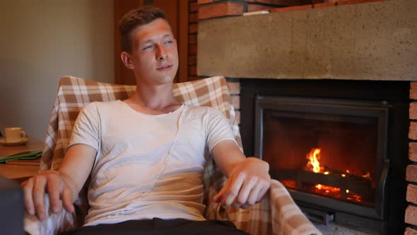 Young Thoughtful Happy Man Admiring Flame Burning in Fireplace in Slow Motion and Looking Away