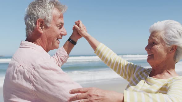 Happy senior caucasian couple talking to each other while dancing on the beach