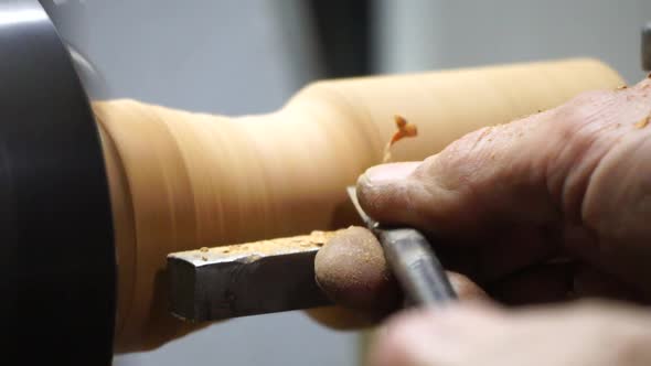 Man Carpenter Using Chisel for Shaping Piece of Wood on Turning Lathe Machine with Many Shavings at