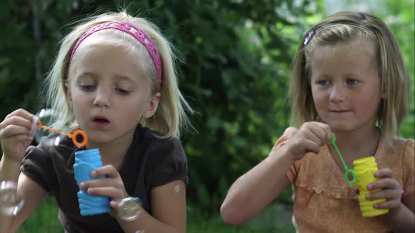 Handheld shot of two little girls blowing bubbles