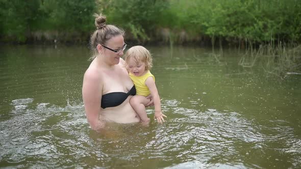 Little Funny Cute Blonde Girl Child Toddler in Yellow Bodysuit Laughing Learns Swim Outside at