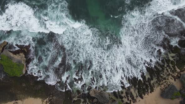 Top down aerial view of giant ocean waves crashing and foaming in coral beach