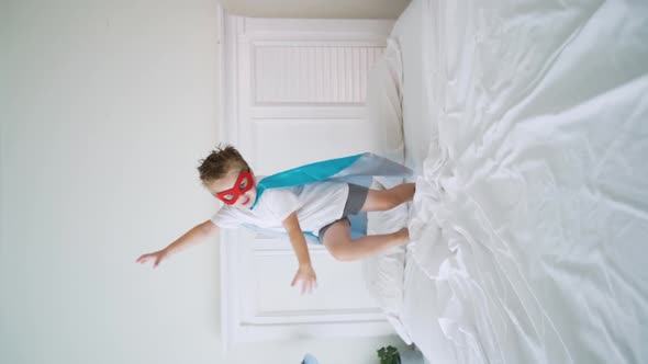 Superhero boy jumping on the bed.