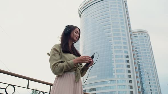 adult girl stands on the street.  wears large headphones and turns on music.