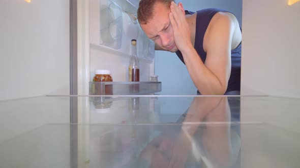 man looks into an empty refrigerator and takes out bottle of alcohol. Alcoholism