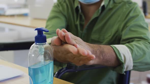 Man wearing face mask sanitizing his hands at office