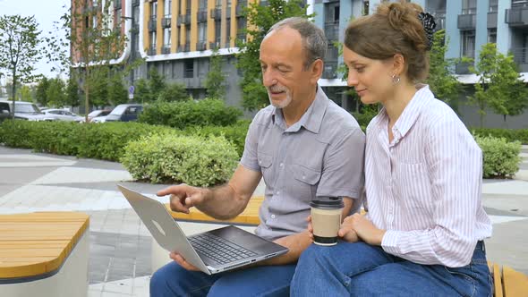 Young Employee is Teaching Her Older Colleague How to Use Laptop and Corporate Software Sitting on