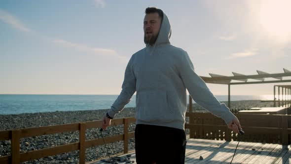 Strong Man Is Jumping Rope Fast Near Pebble Beach in Summer Morning