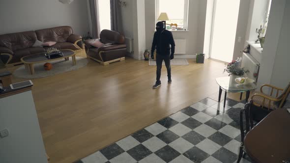The Thief in Black Clothes and Balaclava Walking in the Large Living Room