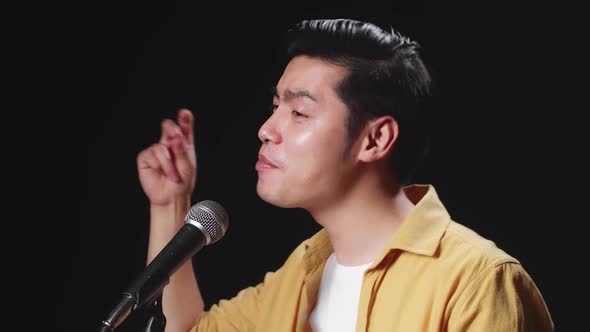 Side View Of Asian Man Singer Singing Into Microphone And Hand Snapping Finger On Black Background