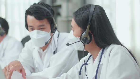 Close Up Of An Asian Man And A Woman Doctors In Masks Working As Call Centre Agent Discussing Work