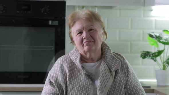 Head And Shoulders Portrait of Happy Senior Woman Sitting in Kitchen at Home