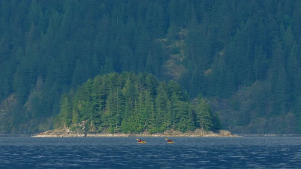 People Canoe Near Small Island In Rugged Landscape