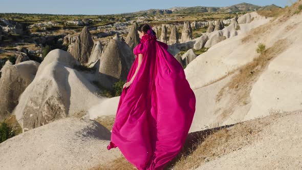 Girl in a Long Purple Dress Stands High on a Rock in Cappadocia